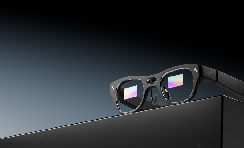 RayNeo X3 Pro glasses resting on a dark reflective surface, showing rainbow-colored displays in both lenses and the dual front camera.